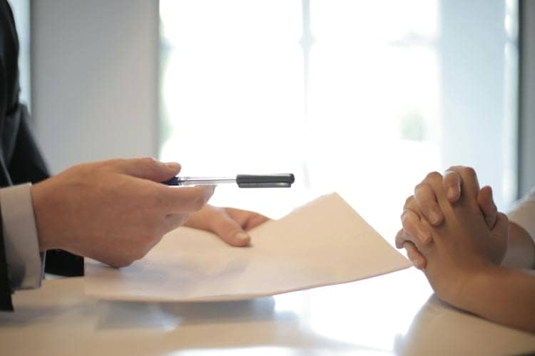 Man's hand holding a pen and business broker agreement over table next to client ready to sell her business.