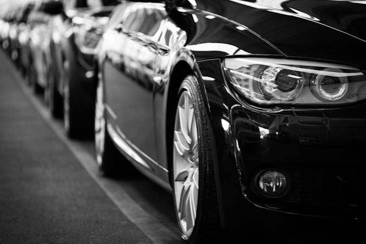 Black and white photo of cars lines up, closeup of headlight.